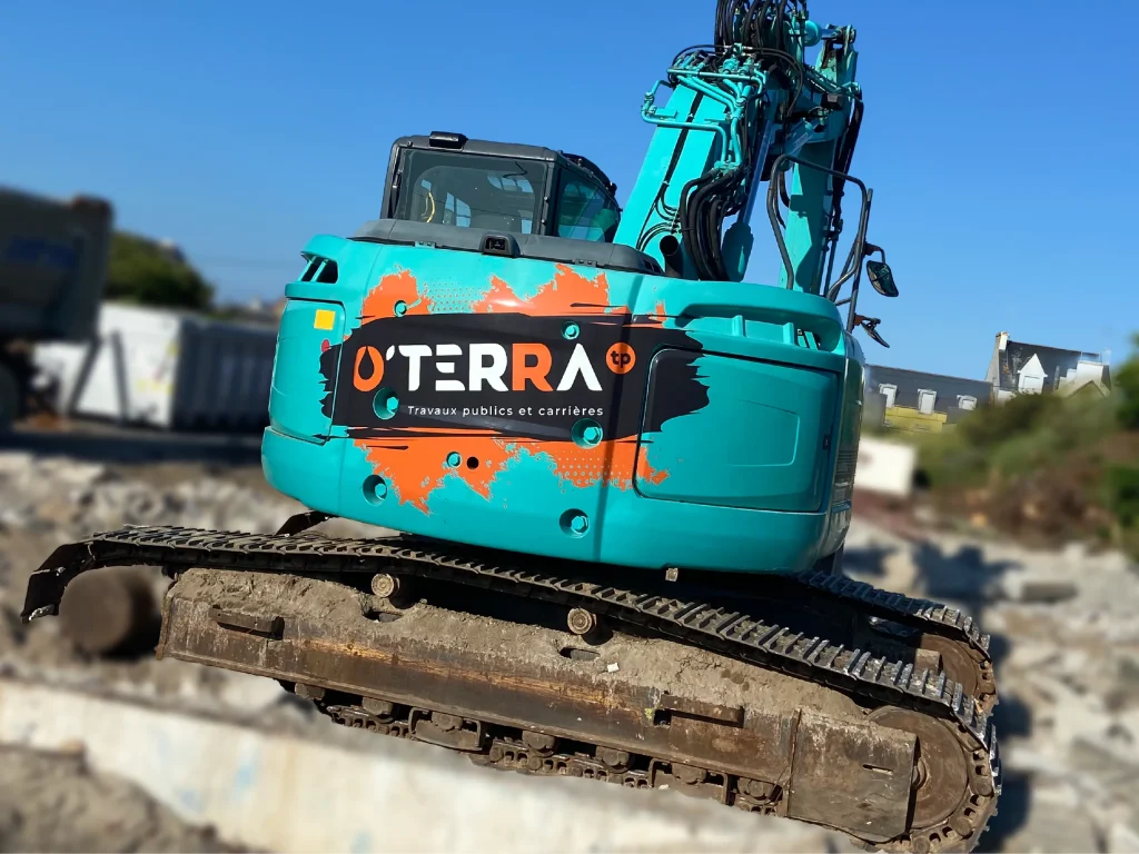 Turquoise excavator with orange and black logo on its side parked on a muddy site against a blue sky